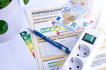 Energiesparend einrichten Zu sehen ist ein Energieausweis, eine Mehrfachsteckdose, und Geld.