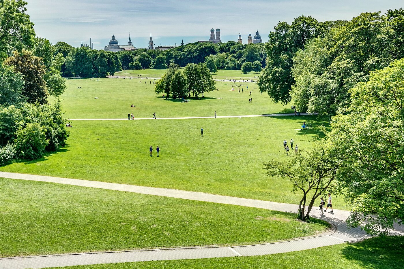 Zu sehen ist der Englische Garten im Vordergrund und die Münchener Skyline im Hintergrund